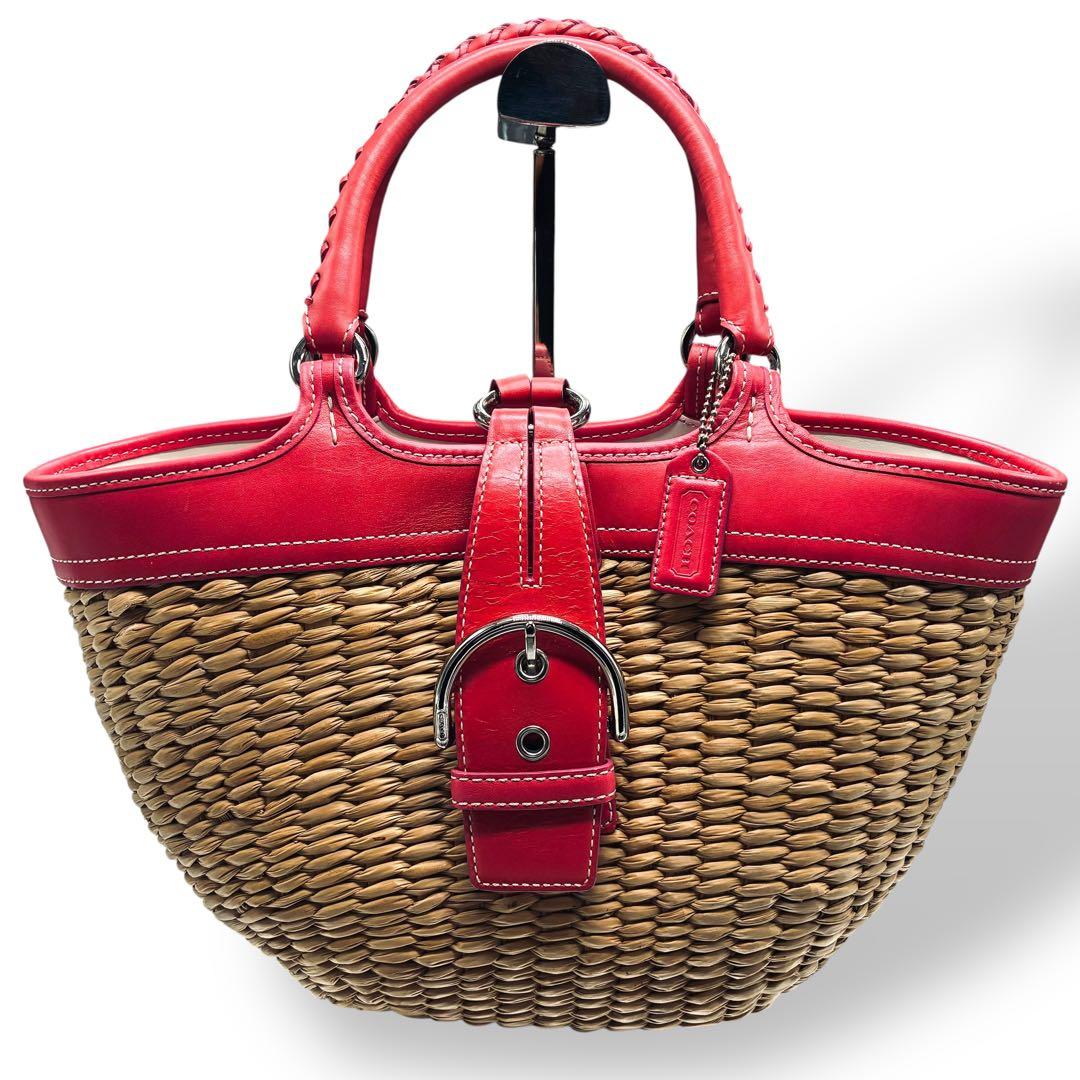 Coach pink and beige straw-woven basket bag with pink leather trim, braided handles, and a front buckle strap.