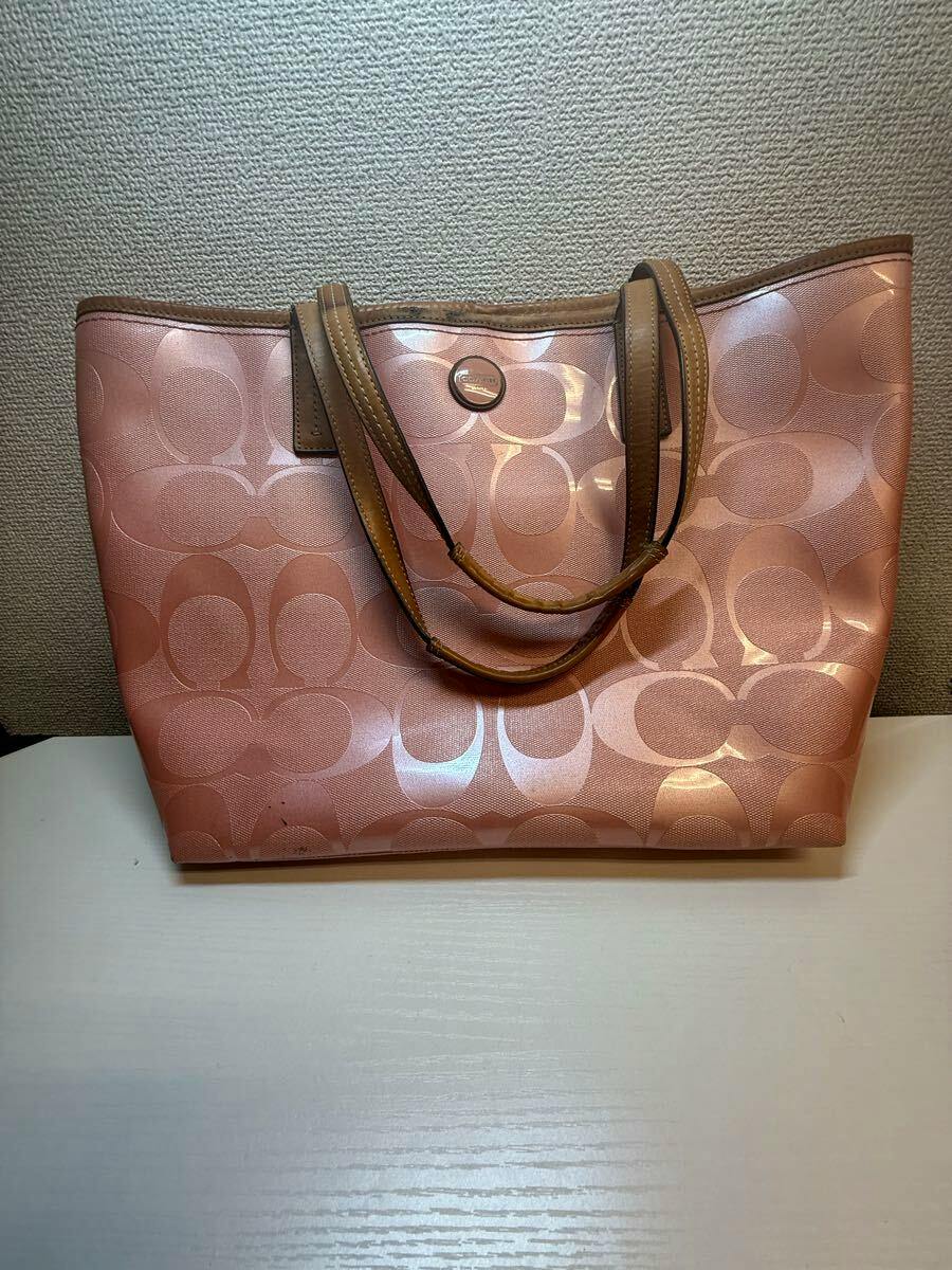 Front view of a pink COACH canvas tote bag with signature C pattern and leather handles.