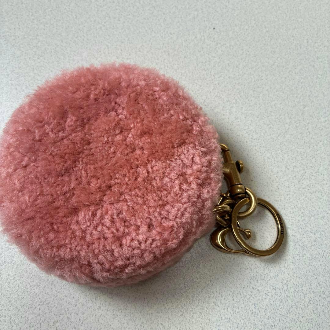 Pink fluffy round Coach keyring pouch with gold keyring and clasp on a light surface.