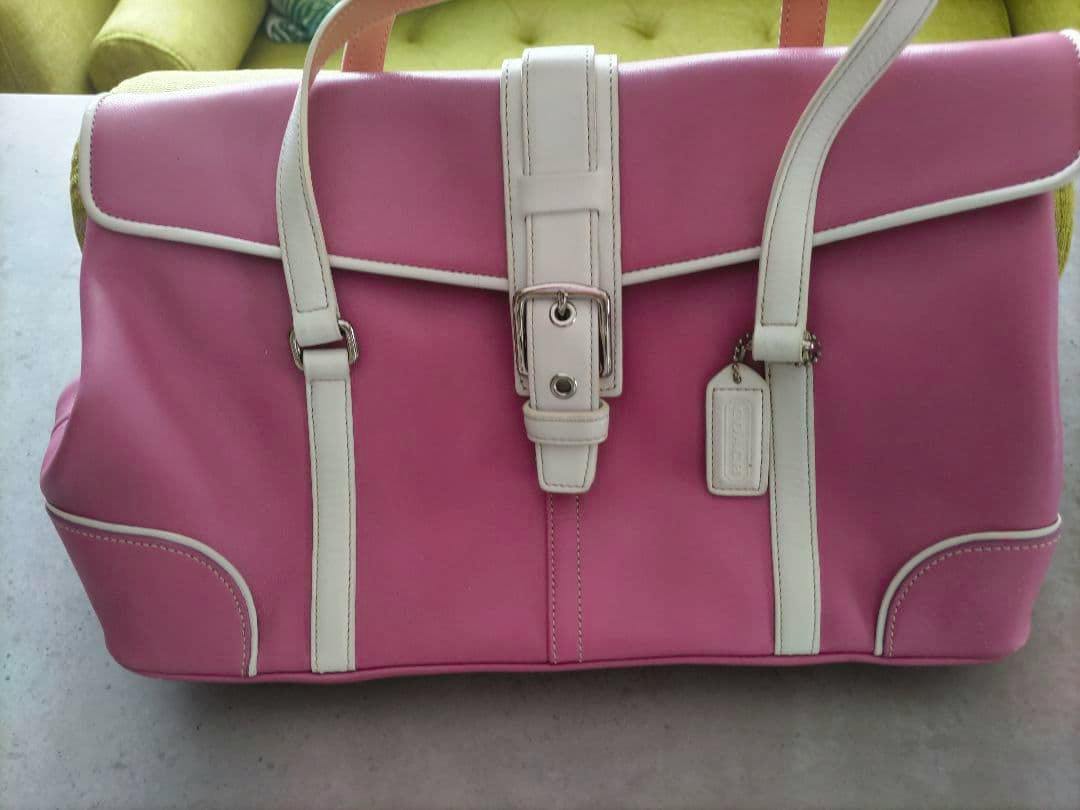 Front view of a pink COACH leather handbag with white trim, center buckle strap, and hang tag.