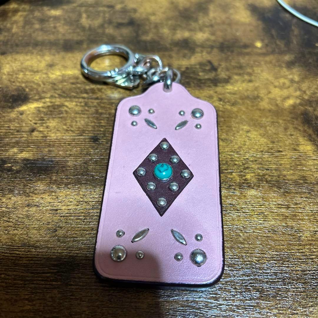 Pink COACH leather keychain bag charm with decorative studs and a turquoise center placed on a wooden surface.