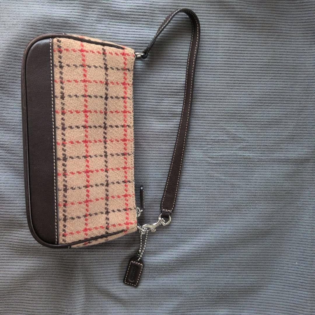 A COACH check-pattern wool handbag with brown leather trim and a short strap lying on a gray ribbed surface.