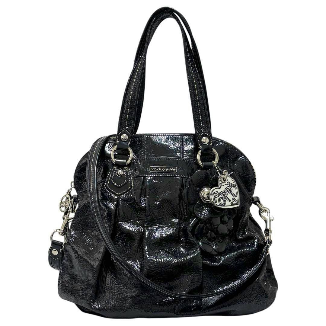 Front view of a black COACH Poppy 2WAY handbag with flower charm and a shoulder strap on a white background.