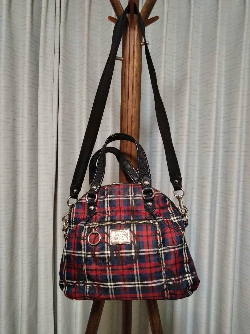 Front view of the check-pattern COACH Poppy 2way shoulder bag hanging on a wooden stand, showing handles, long strap, and front zip pocket.