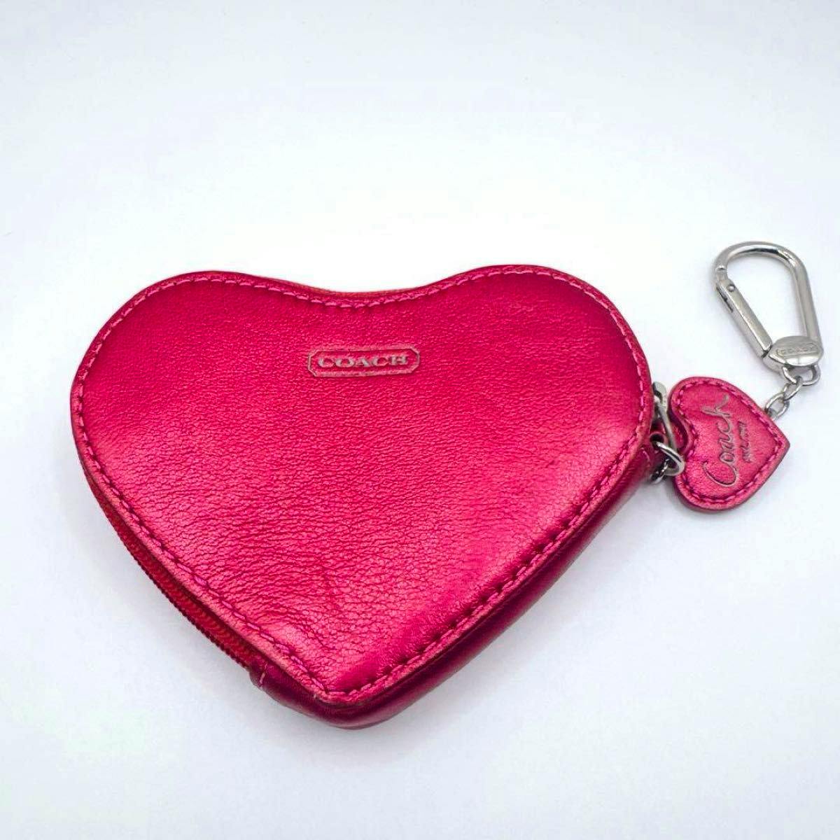 Pink heart-shaped Coach leather coin case with attached heart charm and metal clasp on a white background.
