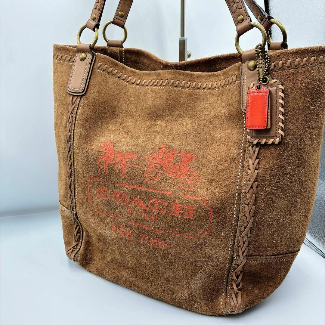 Brown suede COACH tote bag showing the horse-and-carriage logo, braided trim, and an orange leather hang tag.
