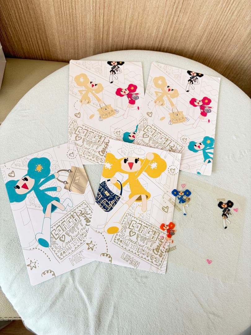 Four Coach Poppy illustrated letter sheets and small character stickers arranged on a round light-blue surface.