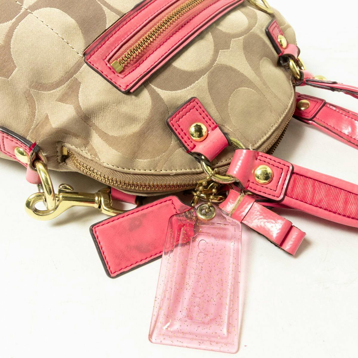 Close-up of a khaki Coach Poppy signature canvas bag showing pink leather trim, gold hardware, and a pink Coach tag.