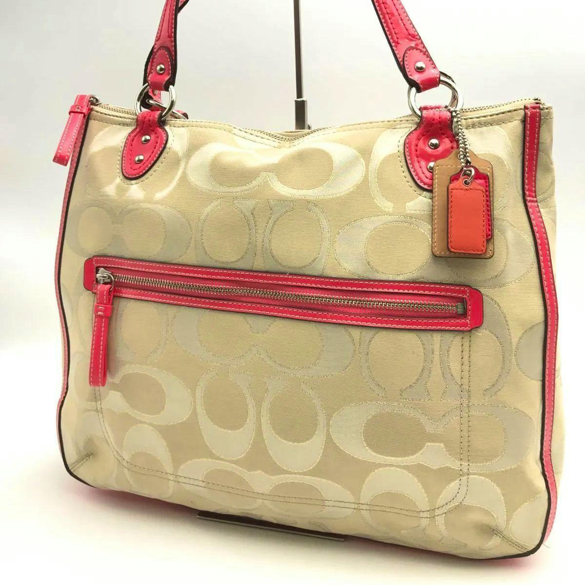 Front view of a beige Coach signature canvas shoulder bag with pink trim and a front zipper pocket.