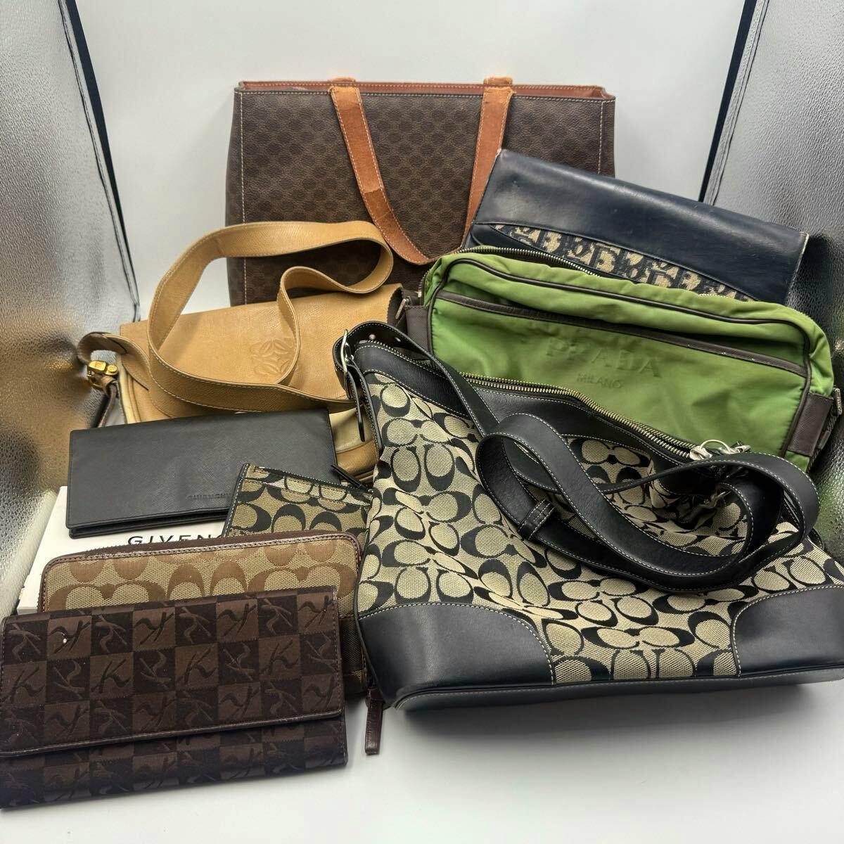 A group of assorted bags and wallets arranged together, including a Coach monogram shoulder bag visible in front.