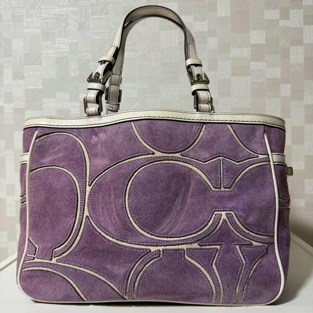 Front view of a purple suede Coach tote bag with cream piping, leather handles, and a Coach hangtag.
