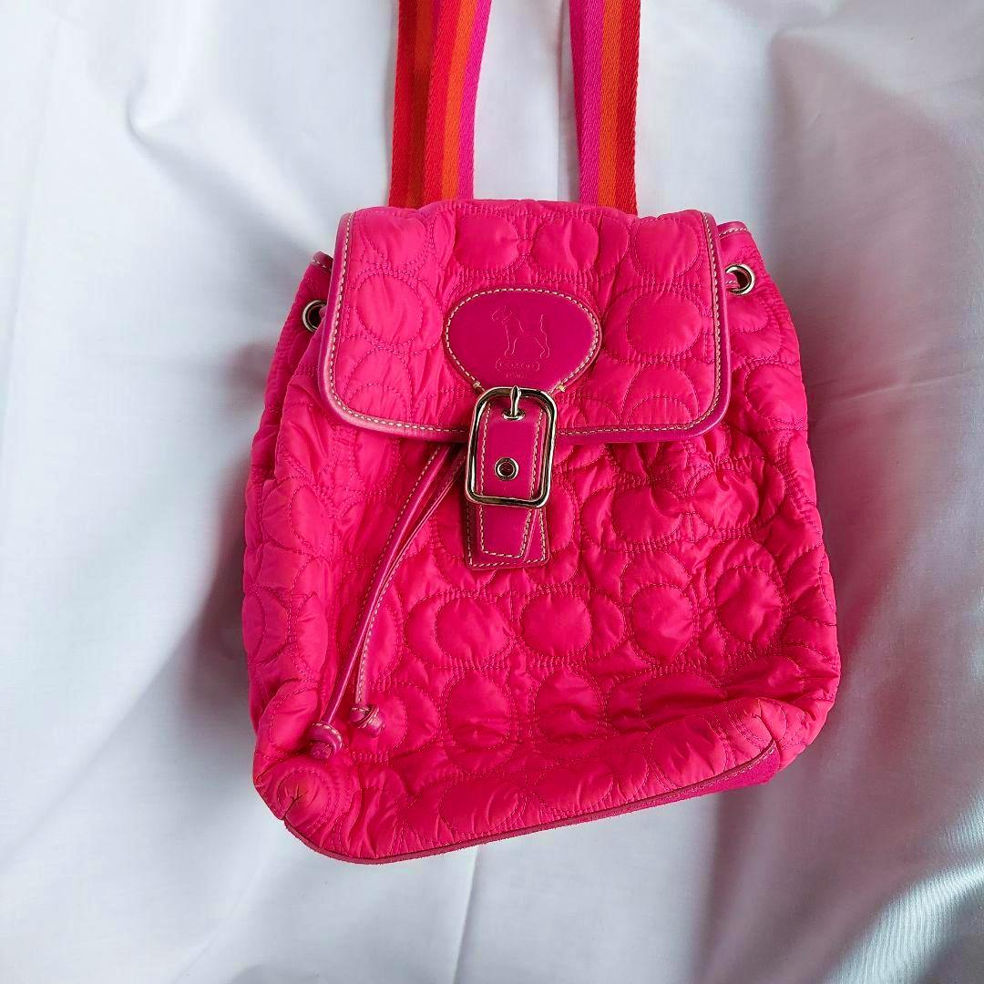 Front view of a pink quilted COACH mini backpack with a flap, buckle, and drawstring.