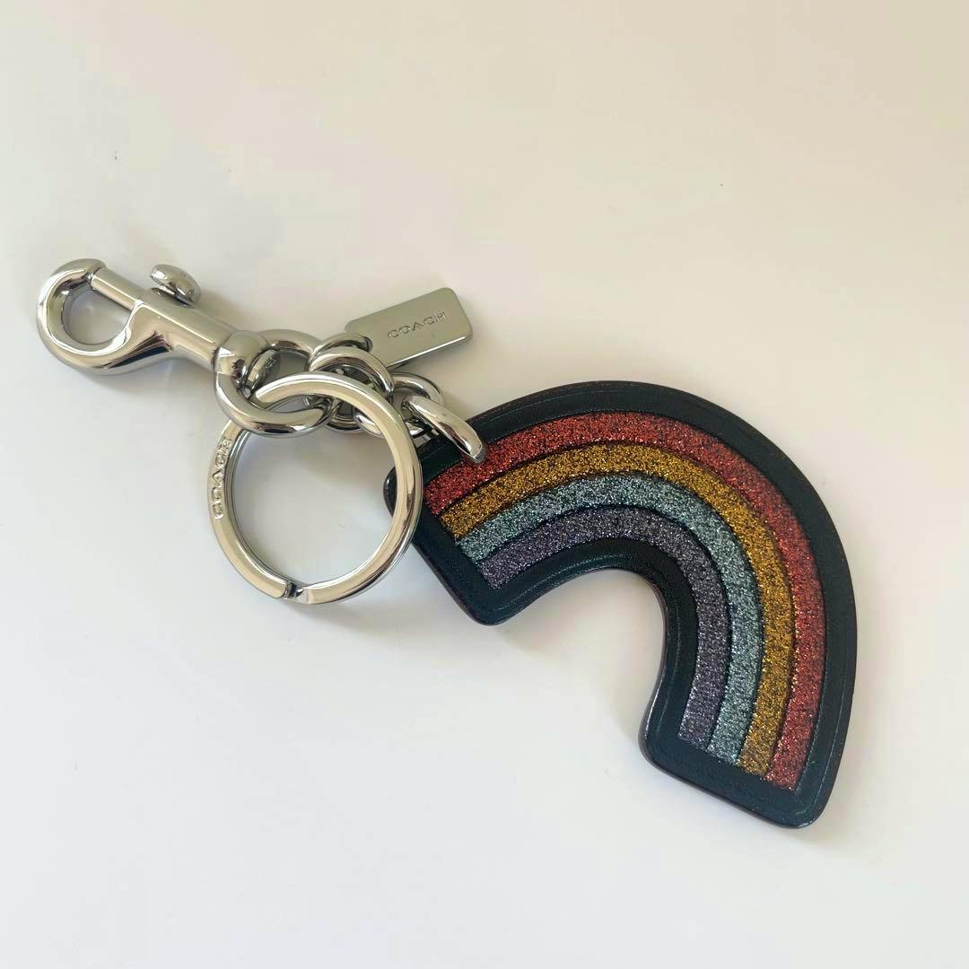 COACH rainbow bag charm keychain in leather with glittery stripes attached to a silver ring and lobster clasp on a white background.