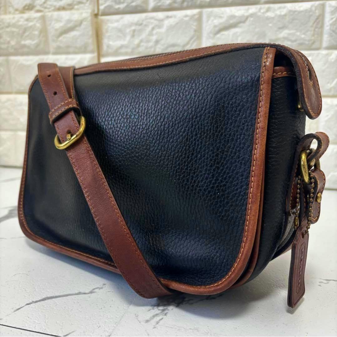 Black pebbled leather Coach shoulder camera bag with brown leather trim, adjustable strap, and Coach hang tag visible.