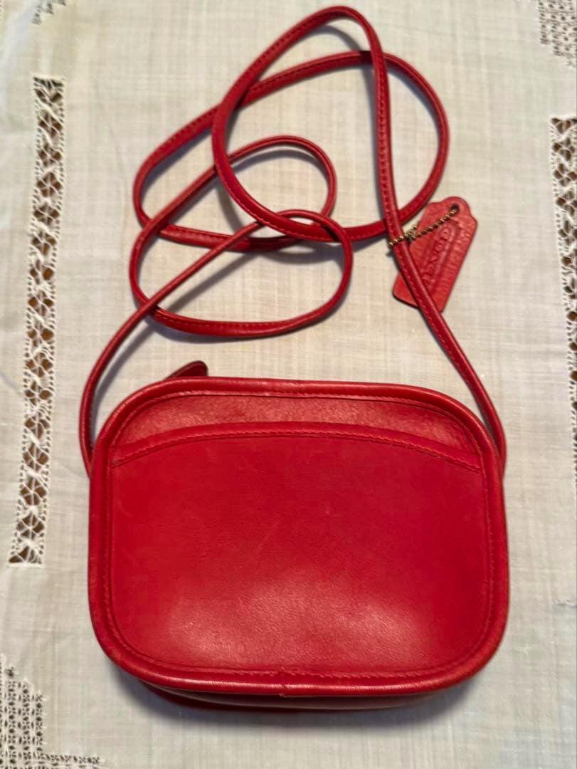 Front view of a red Coach leather shoulder bag laid flat, showing the long strap and leather tag.