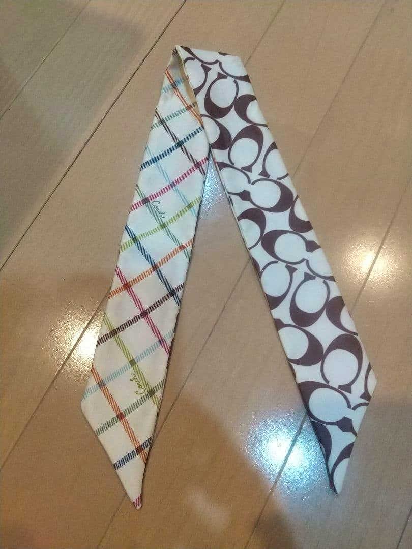 Reversible Coach silk scarf laid flat showing a multicolored check side and a brown Coach 'C' pattern side on a wooden floor.