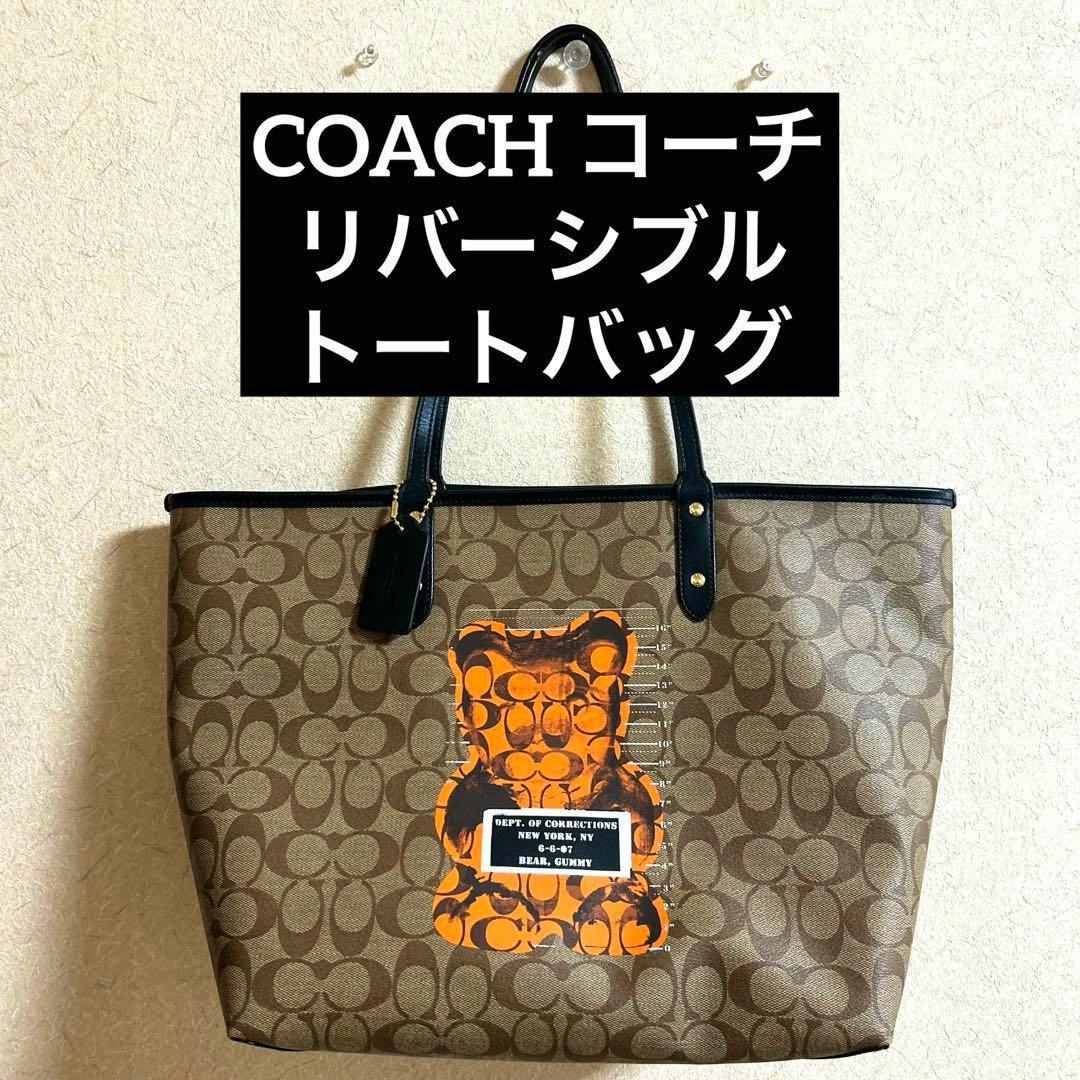Brown Coach reversible tote bag with signature C pattern and an orange bear graphic hanging on a wall.