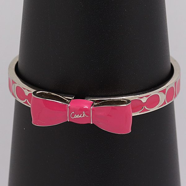 Silver-tone Coach bangle bracelet with a pink enamel bow displayed on a black jewelry cone.
