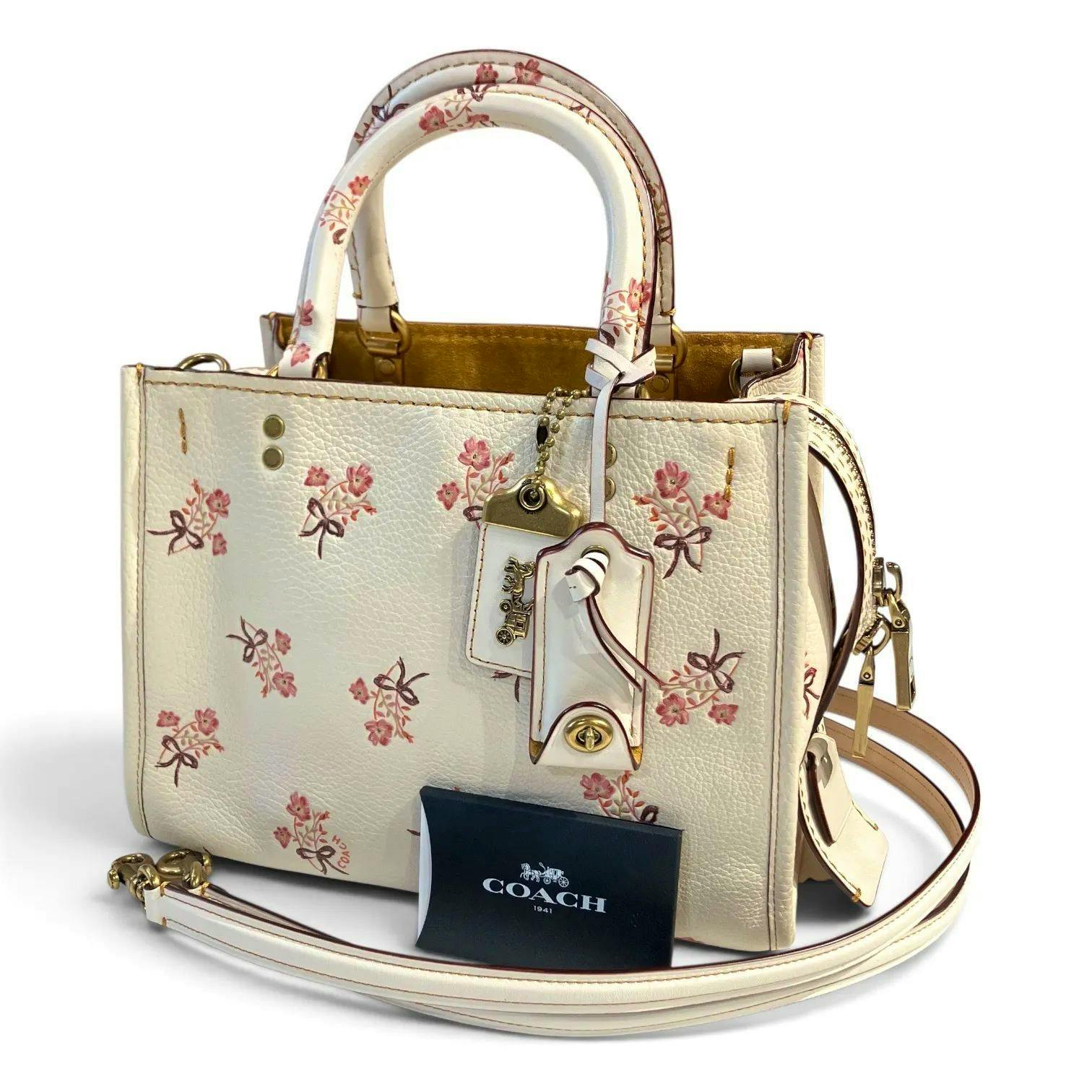 White and pink Coach Rogue 25 cow leather handbag with floral bow print, top handles, shoulder strap, and Coach tag.