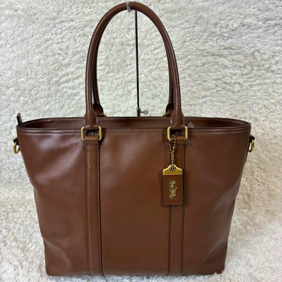 Front view of the brown COACH Rogue Metropolitan cow leather tote bag with two handles and a hanging logo tag.