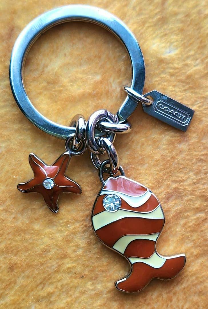 COACH keyring bag charm with an enamel fish and a starfish charm on a yellow background.