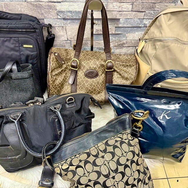 A set of seven assorted handbags and backpacks displayed together, including a Coach-pattern fabric shoulder bag placed in front.