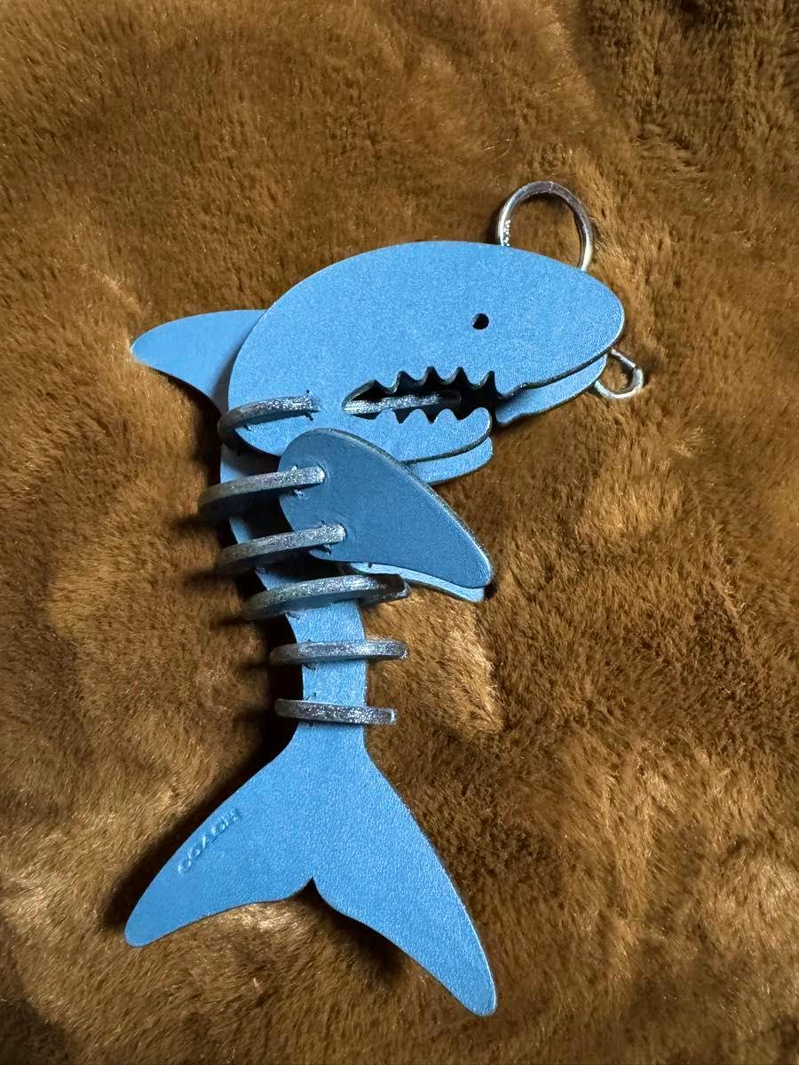 Blue shark bag charm keyring with segmented body and metal rings lying on a brown fur background.