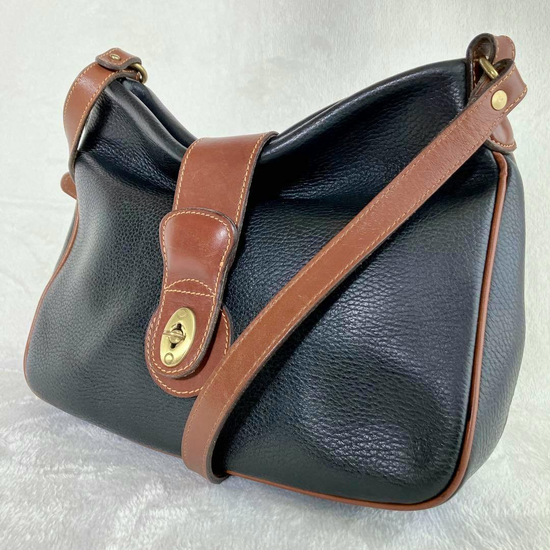 Coach Sheridan turnlock leather shoulder bag in black with brown trim and a brass turnlock shown at an angle.