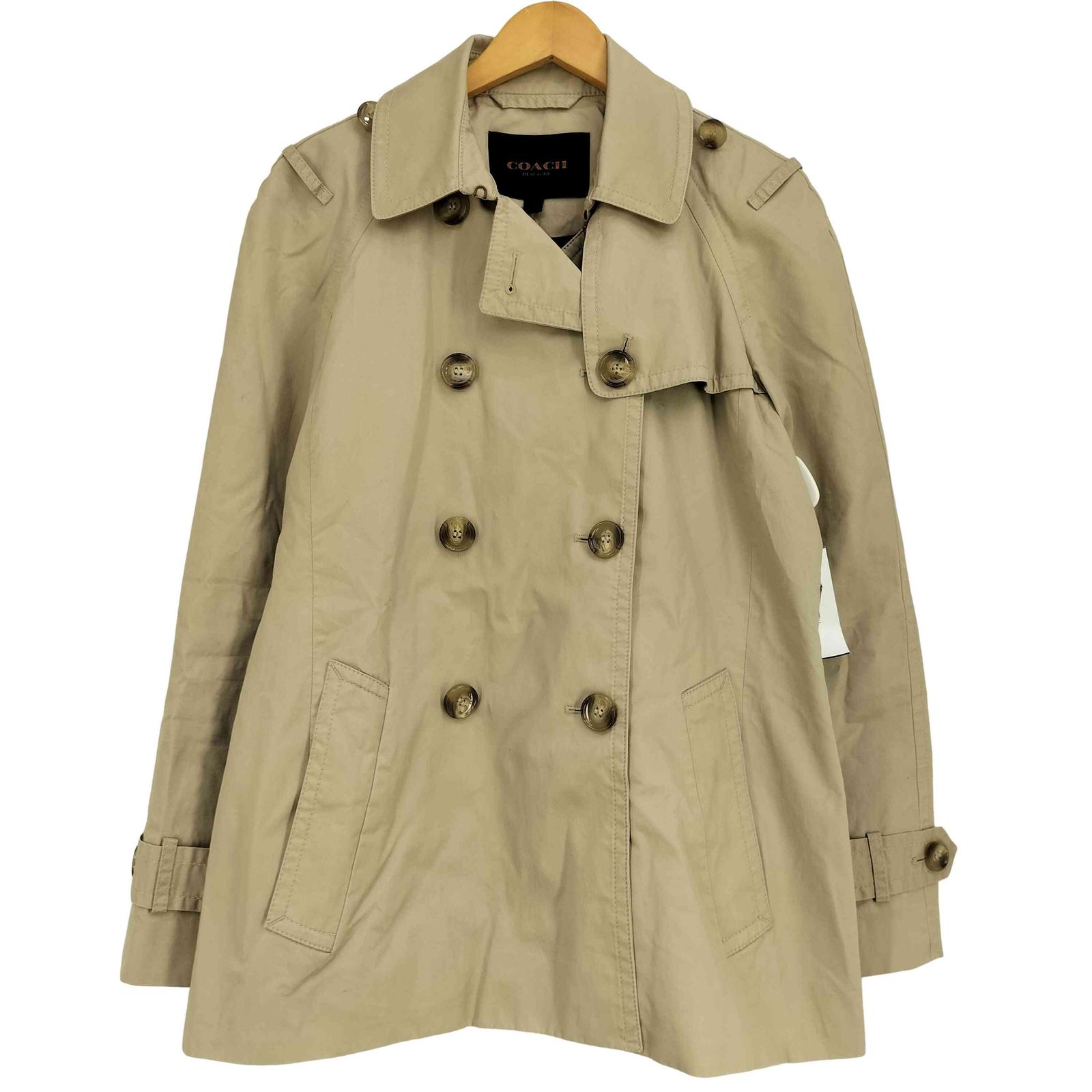 Front view of a beige COACH short trench coat on a hanger with double-breasted buttons and front pockets.