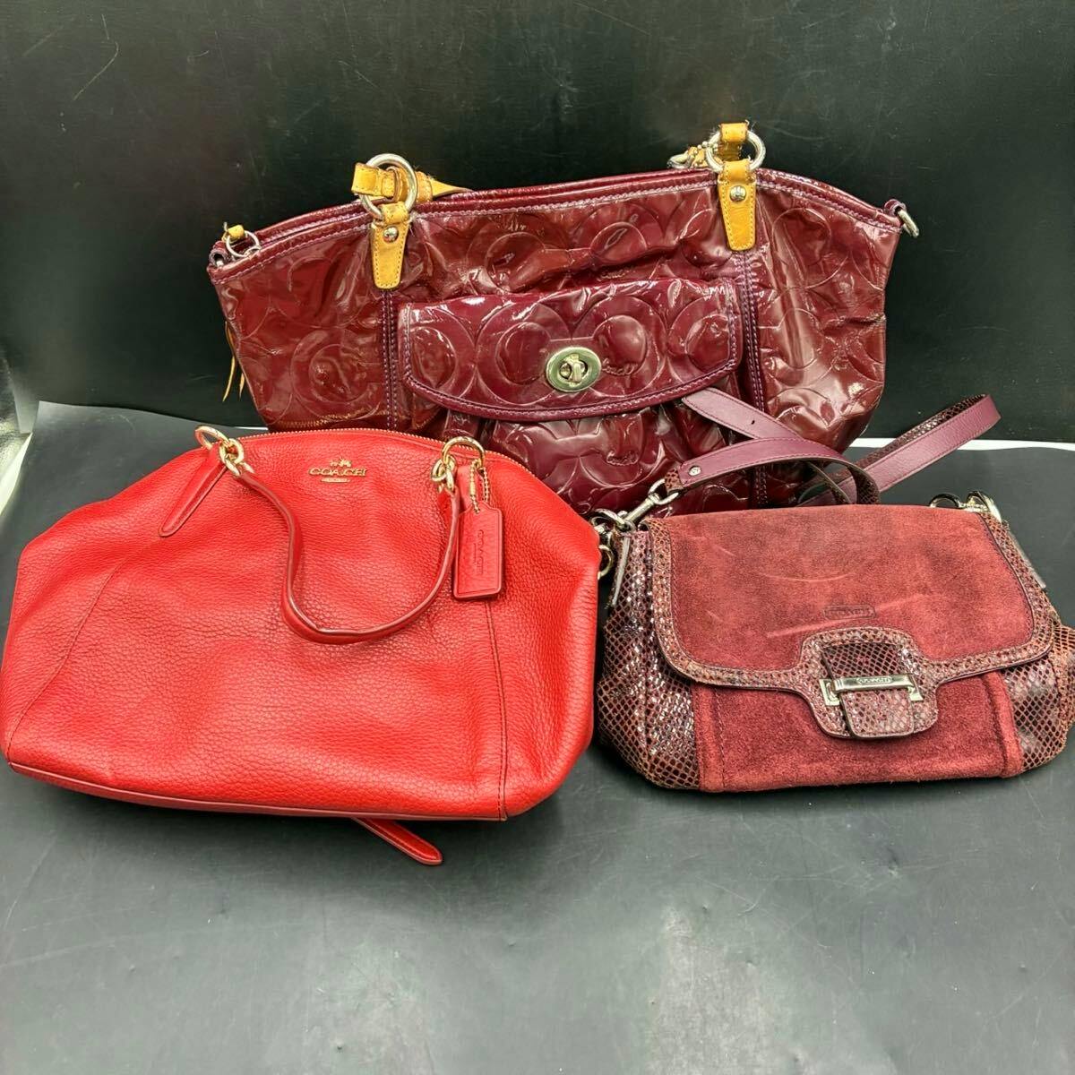 Three COACH red and burgundy shoulder and hand bags displayed together on a black surface.