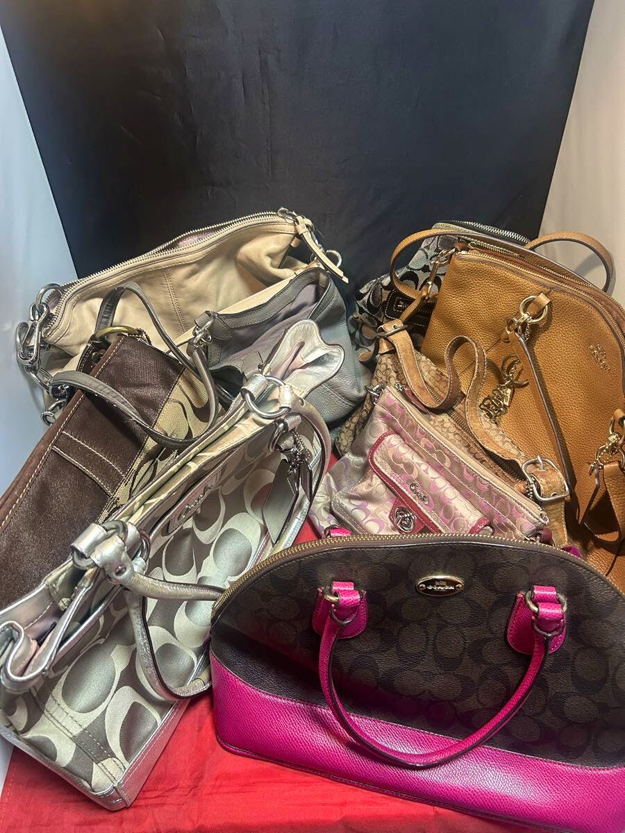 A pile of multiple COACH shoulder and tote bags in various colors and patterns displayed on a red surface.