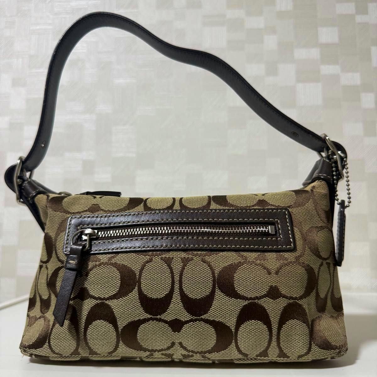 Front view of a brown Coach canvas shoulder bag with signature 'C' pattern, leather trim, front zip pocket, and short leather strap.