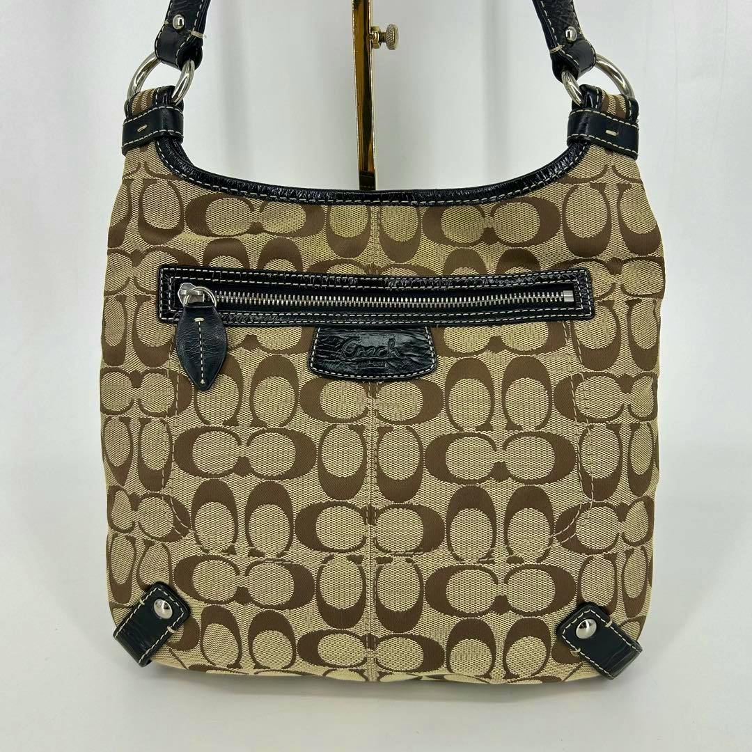 Front view of a Coach canvas shoulder bag with signature 'C' pattern and a front zip pocket.
