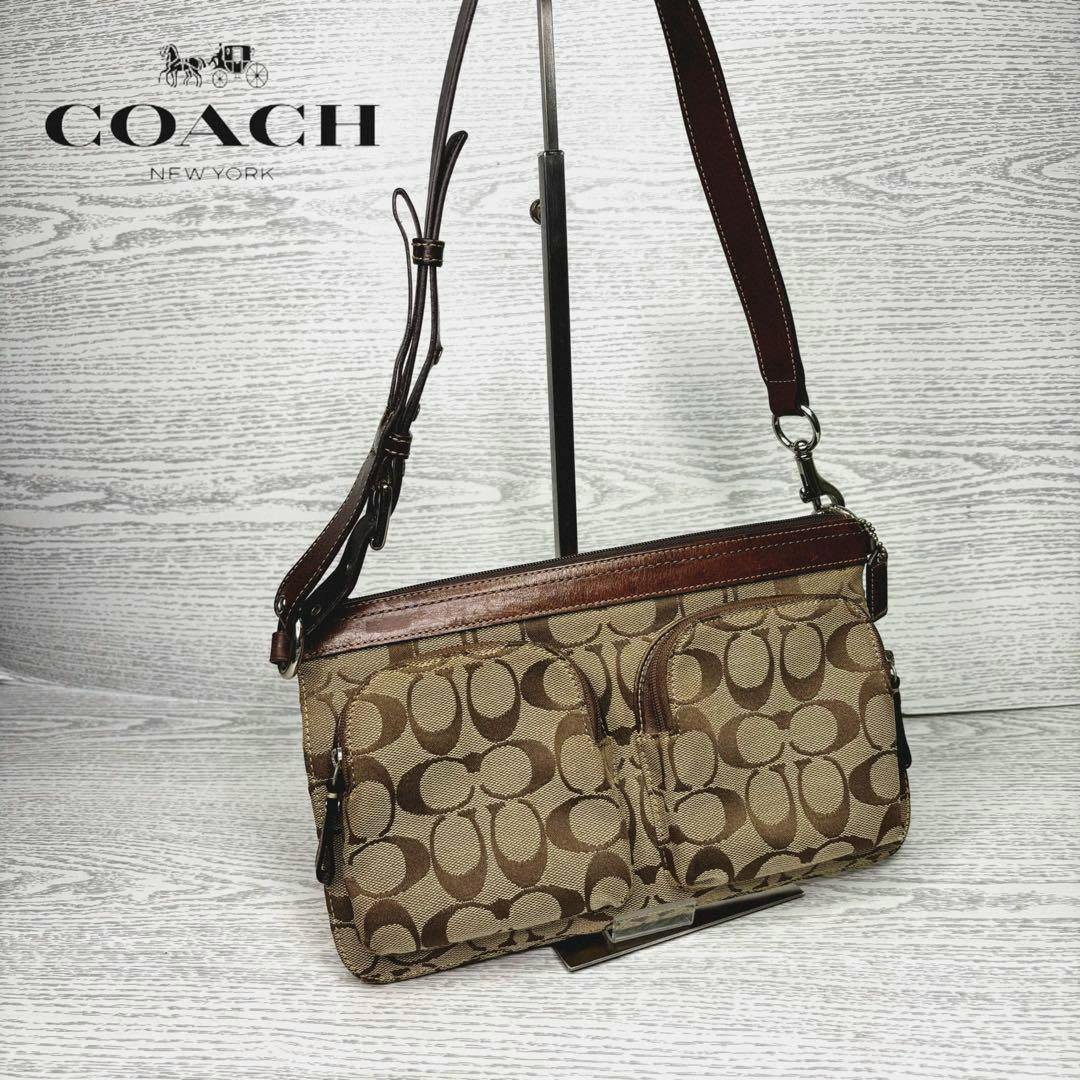 Brown COACH canvas shoulder bag with signature 'C' monogram and leather trim hanging from a stand.