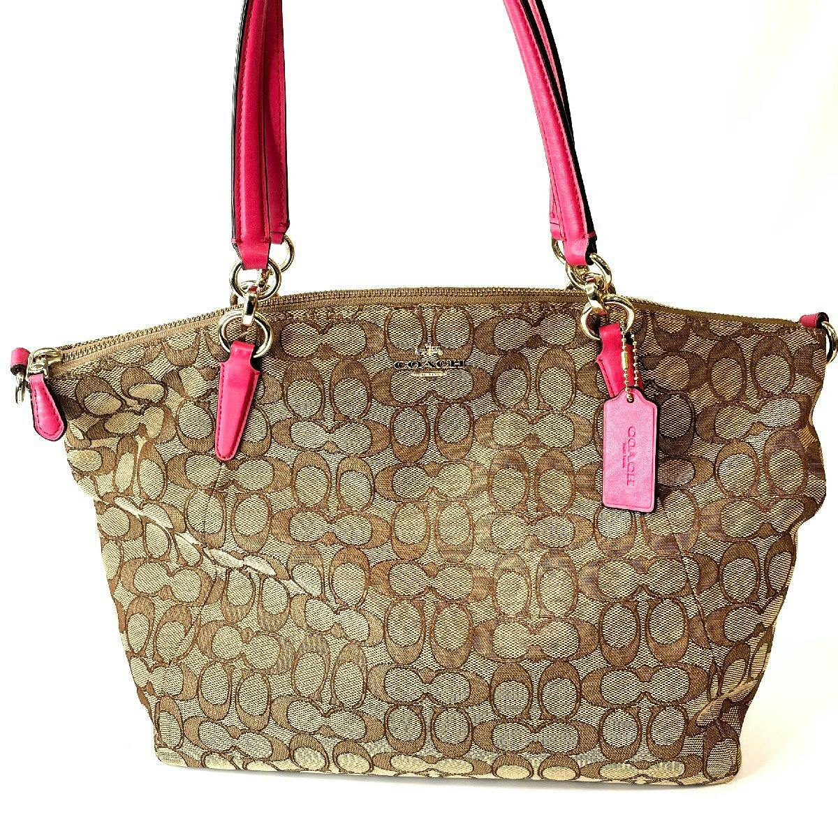 Beige Coach signature canvas handbag with pink handles, pink tag, and gold hardware visible from the front.