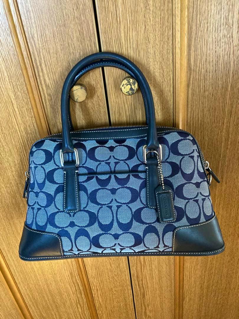 Blue Coach signature canvas 2WAY mini Boston handbag with leather handles hanging on a wooden door.