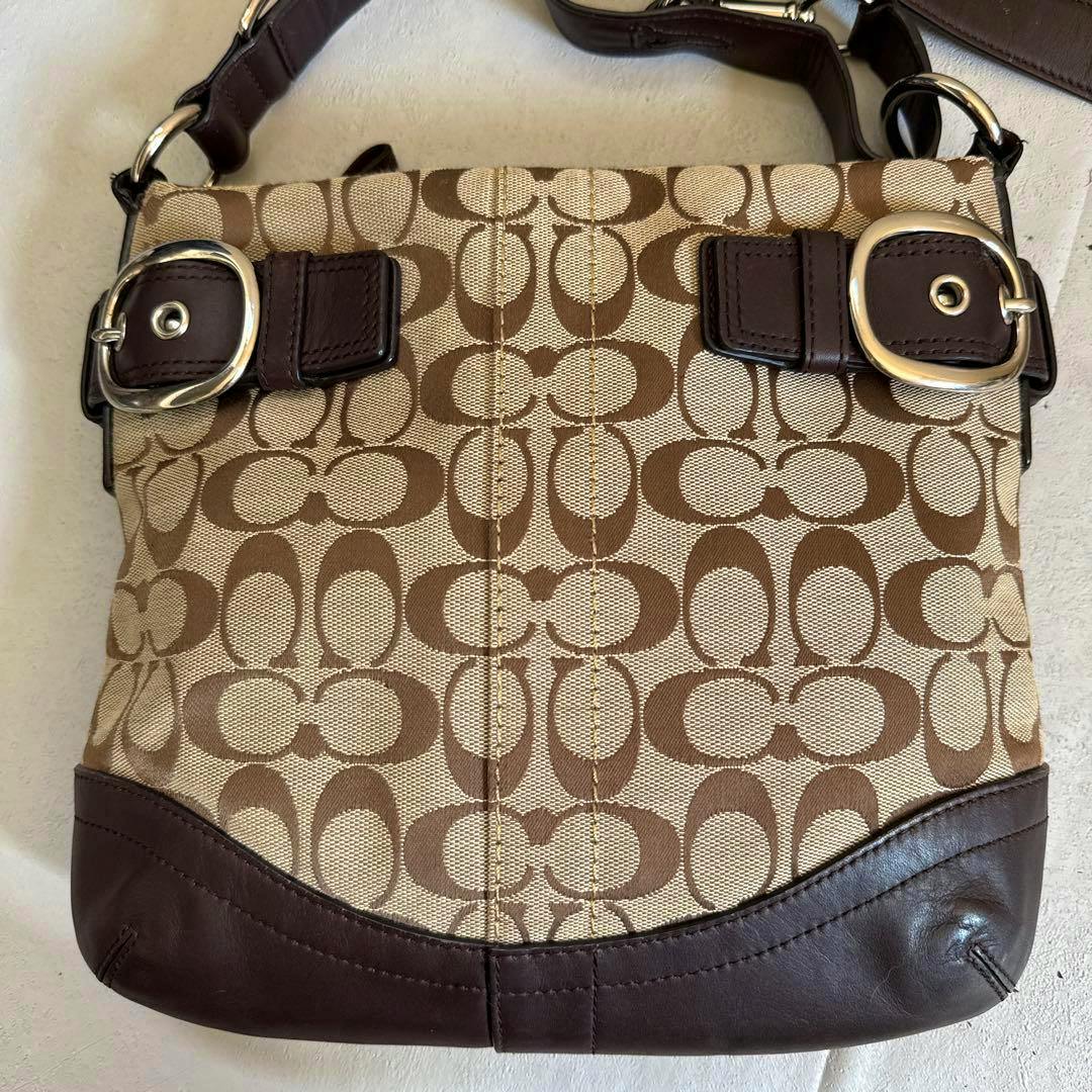 Front view of a brown Coach signature canvas shoulder bag with leather trim, dual buckles, and a shoulder strap.