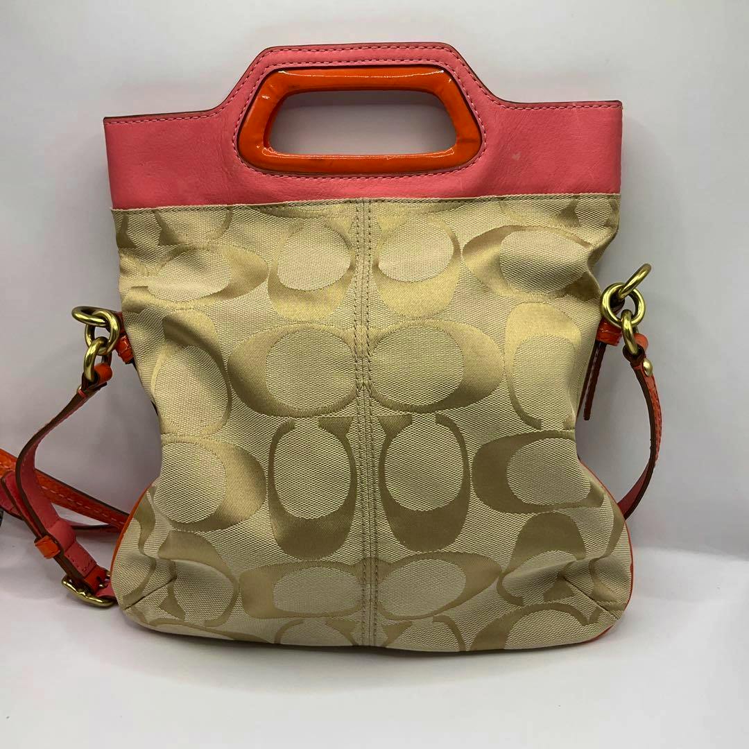 Front view of a Coach canvas 2way shoulder bag with beige signature 'C' pattern, pink upper trim and orange handle detail.