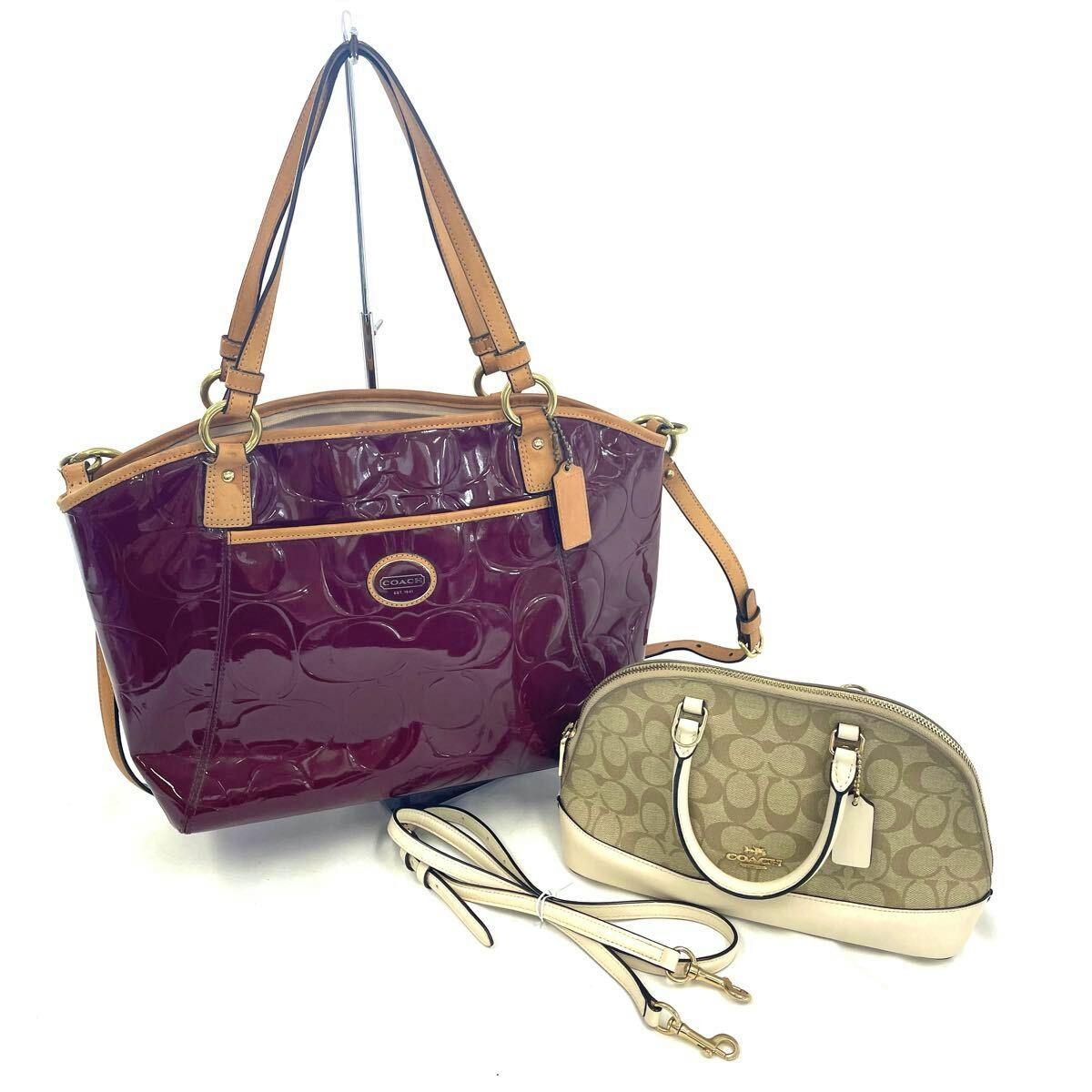 Two Coach bags: a red patent signature tote with tan leather trim and a beige Coach signature mini handbag with detached straps.