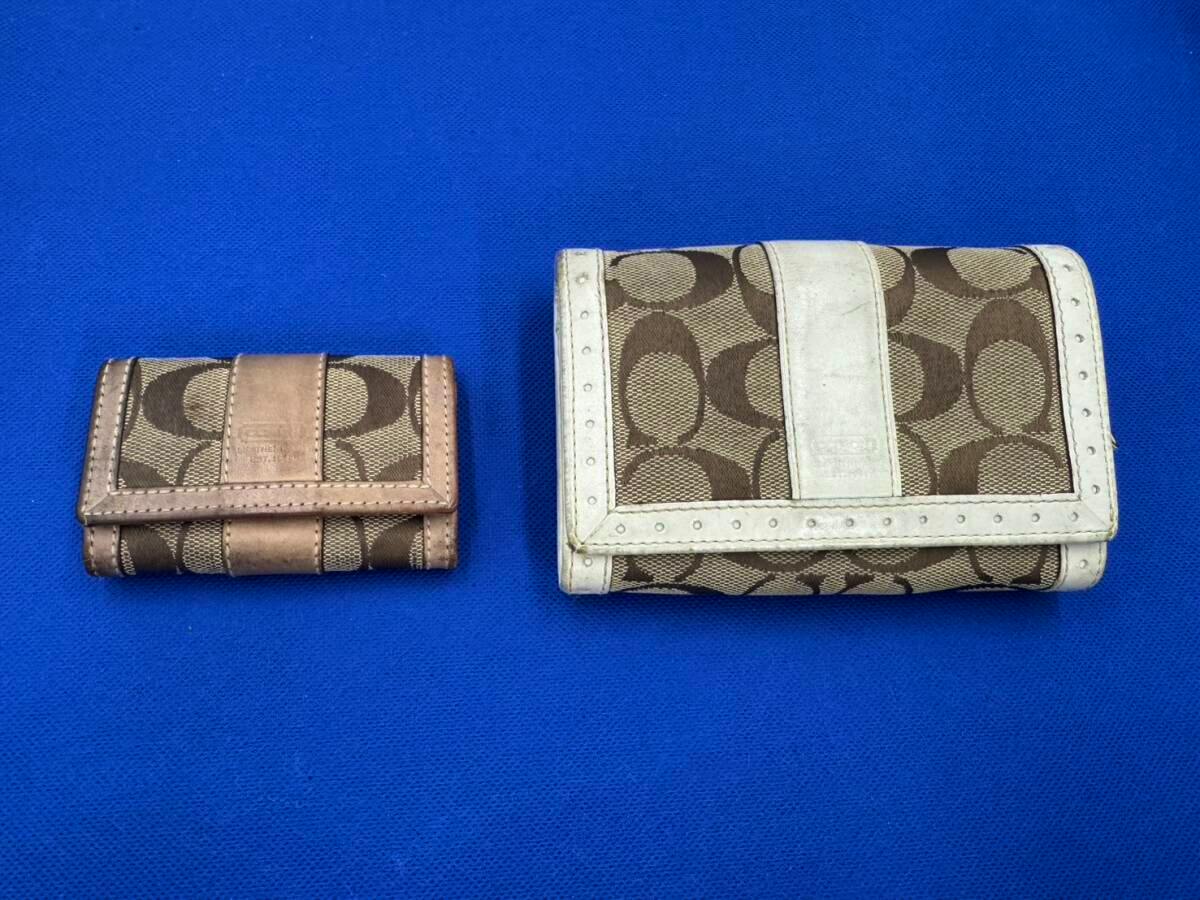 Two Coach signature canvas items — a small brown key case and a larger brown-and-white wallet — placed on a blue background.