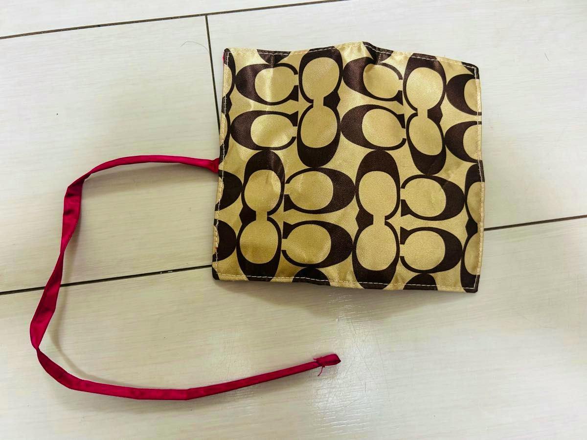 Brown Coach signature-pattern accessory pouch with a long pink ribbon strap lying flat on a light floor.
