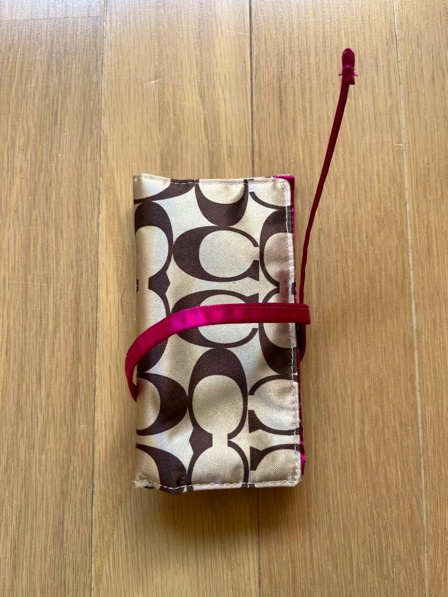 Folded Coach signature-pattern accessory case with brown monogram print and a pink ribbon laid on a wooden floor.