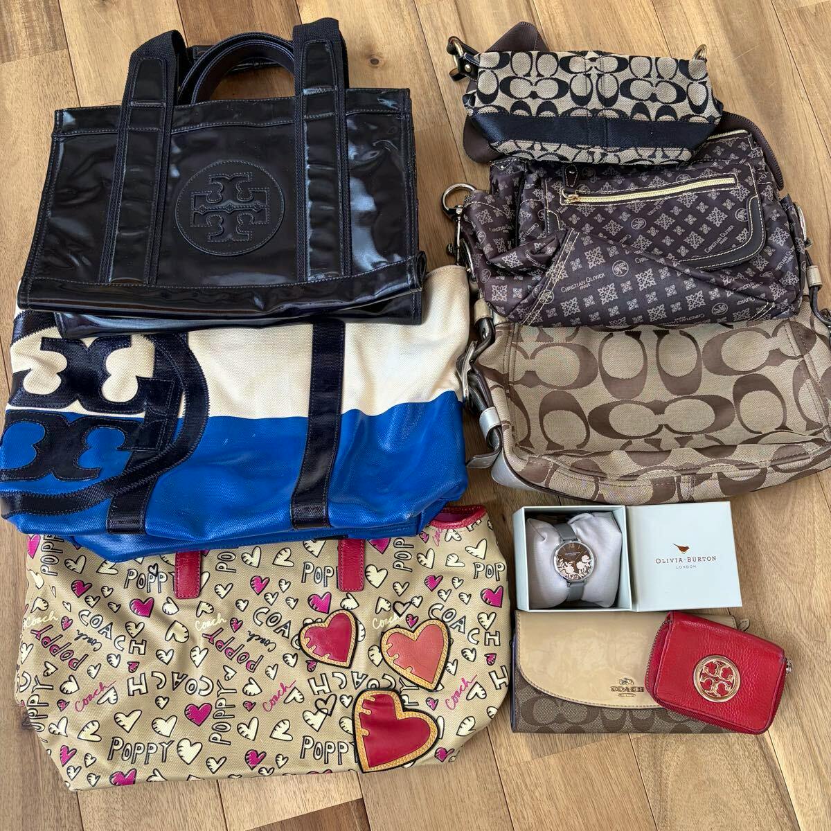 Several Coach and other branded tote and shoulder bags with small accessories arranged on a wooden floor.