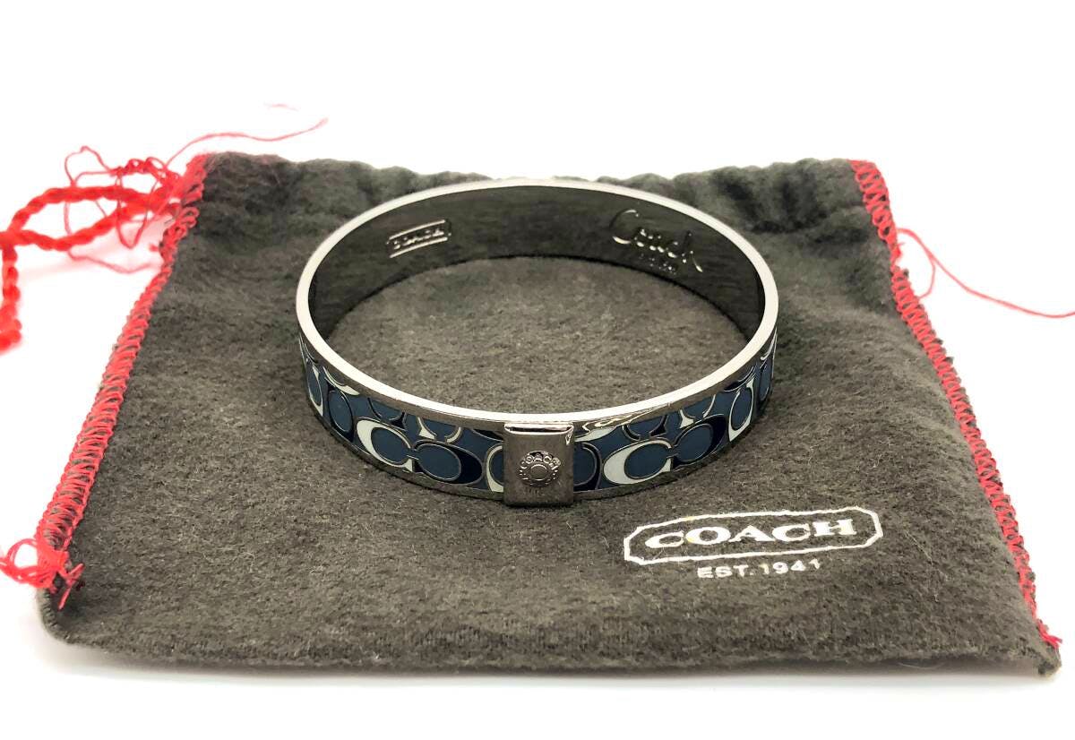 Coach signature bangle bracelet with blue 'C' pattern resting on a gray Coach drawstring pouch.