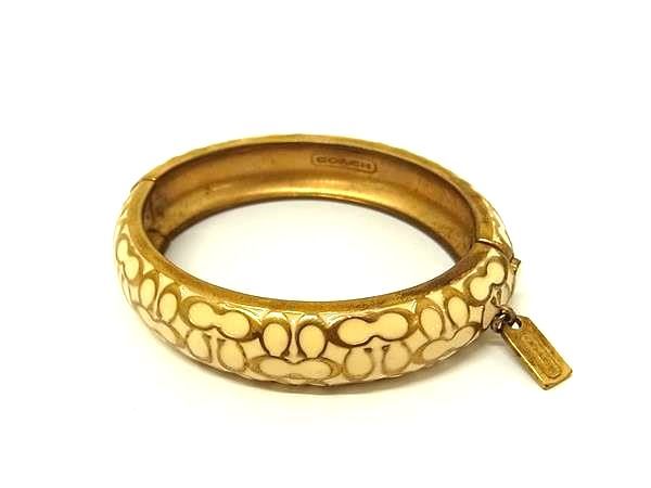 Gold-plated Coach signature bangle with ivory-colored pattern and a small rectangular tag on a white background.