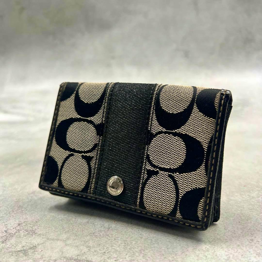 Front view of a COACH signature black canvas card holder with snap closure and signature 'C' pattern.
