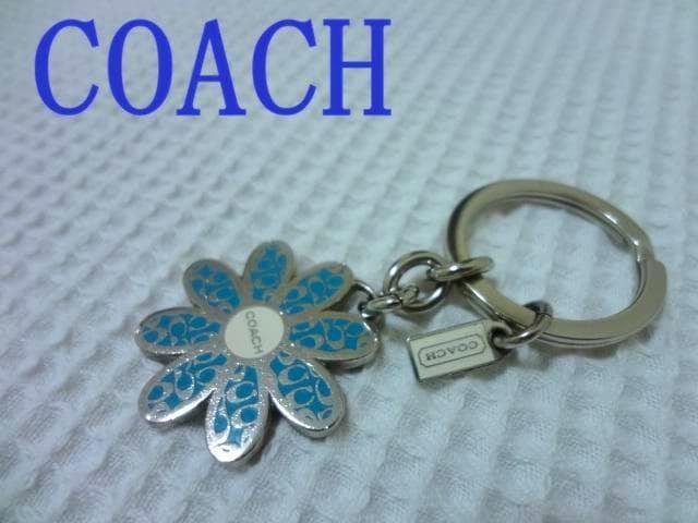 Close-up of the COACH flower bag charm keyring with blue signature pattern and COACH logo on a white textured background.