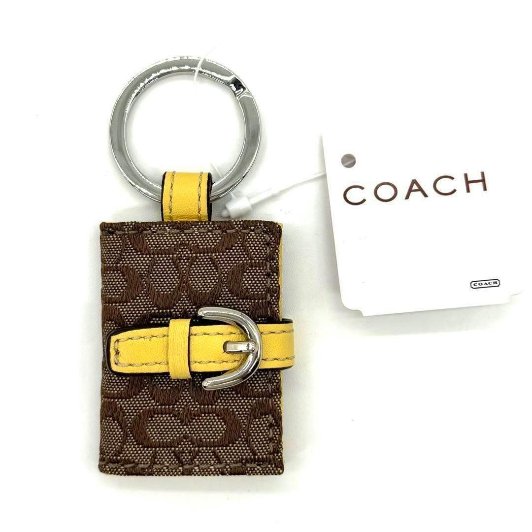 COACH signature book photo keychain in brown jacquard with a yellow leather strap buckle and silver keyring.