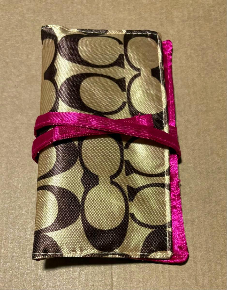 Folded COACH signature-pattern accessory pouch with a pink ribbon tie on a plain surface.