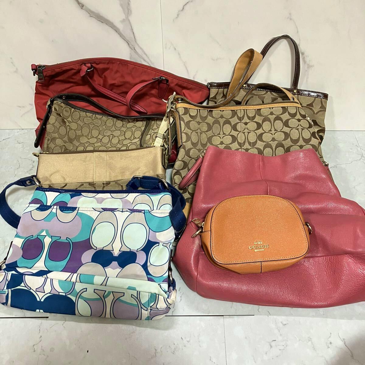 A group of Coach canvas and leather handbags and shoulder bags in various colors and signature patterns arranged on a tiled floor.